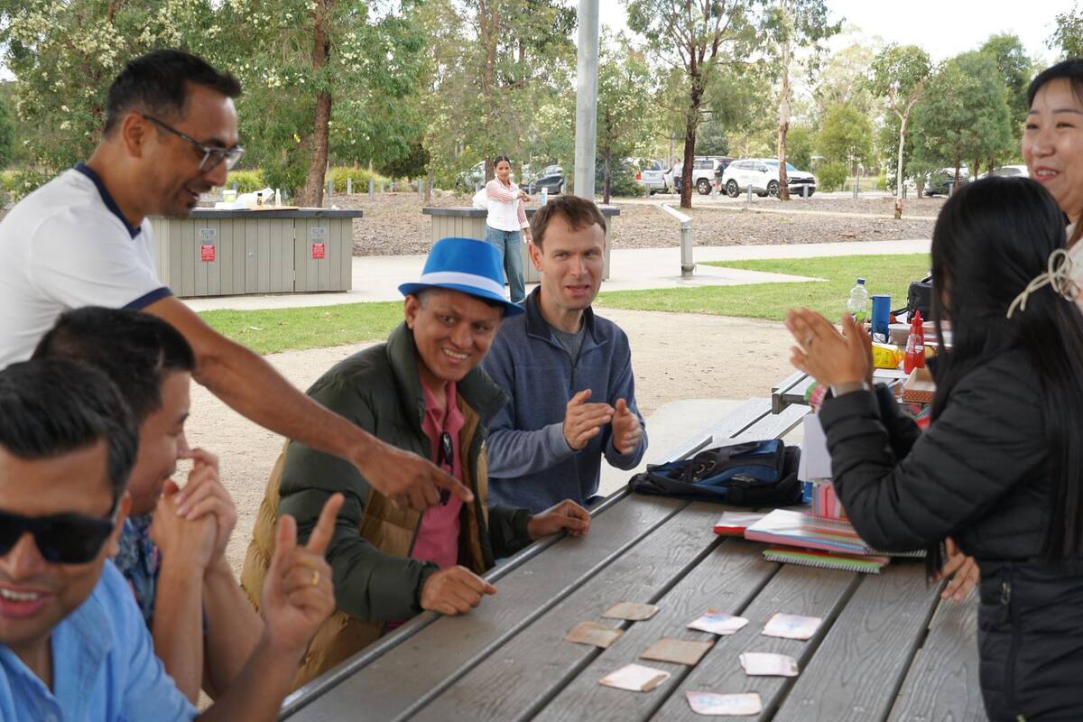 Enable Hub support workers and participants laughing over a card game at a park picnic table